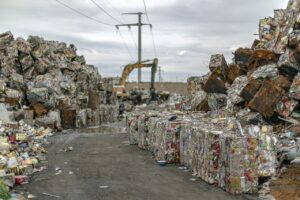 News & Announcements Large scrap yard with compressed metal waste blocks and excavators used for recycling operations.